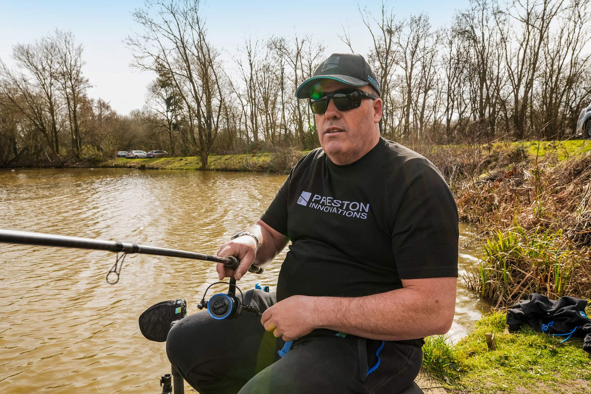 Preston Lightweight Black Raglan T-shirt – visser draagt het zwarte T-shirt met Preston-logo aan de waterkant