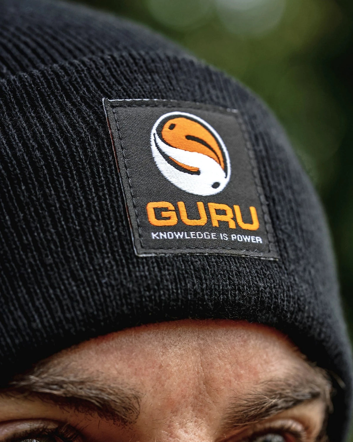 Guru Black Patch Beanie – close-up van de geborduurde oranje-witte Guru-patch en het fijne zwarte breisel