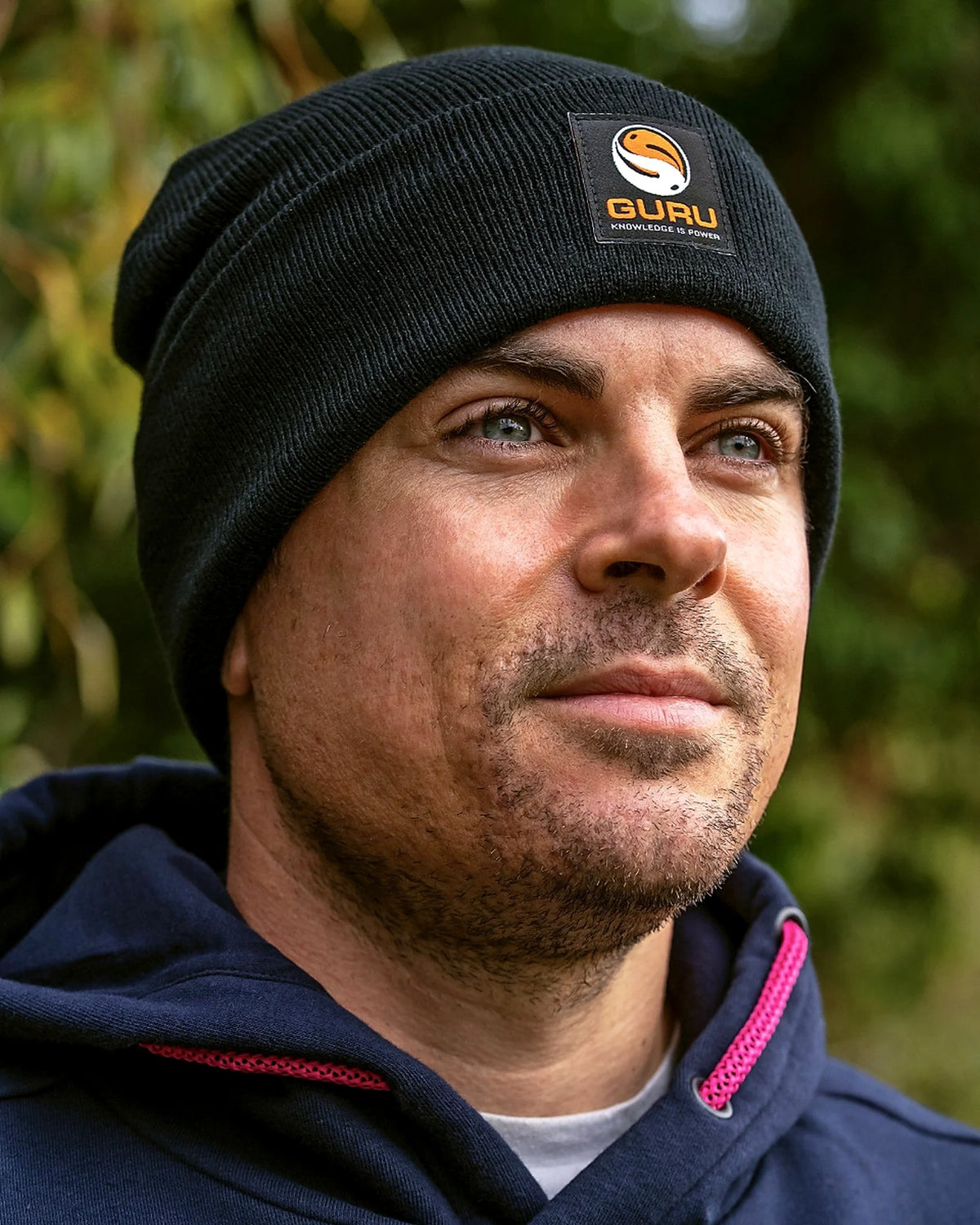Guru Black Patch Beanie – gedragen buiten met zichtbare Guru-patch tegen een groene achtergrond