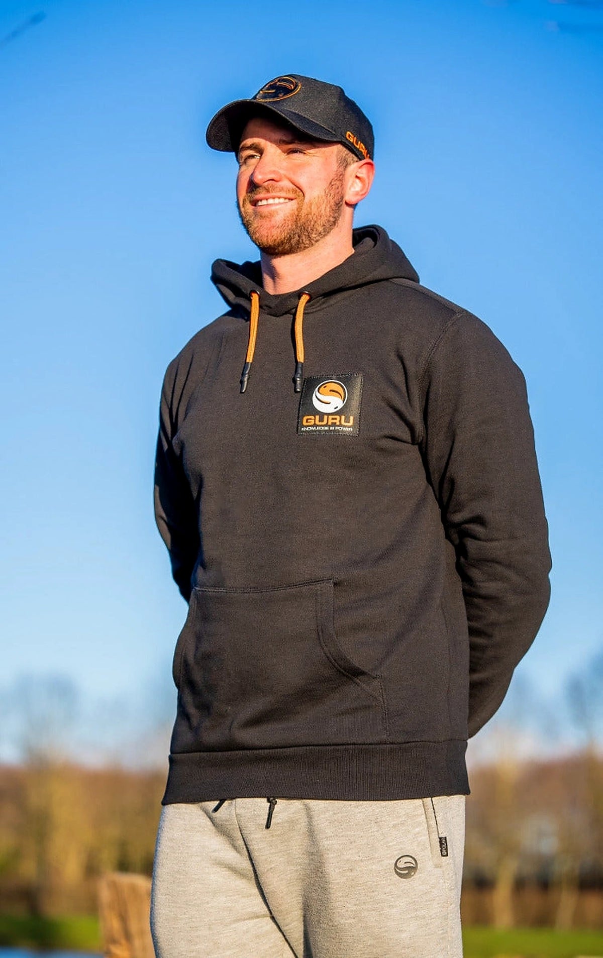 Guru Black Patch Hoodie – gedragen vooraanzicht buiten met oranje koorden en borstpatch