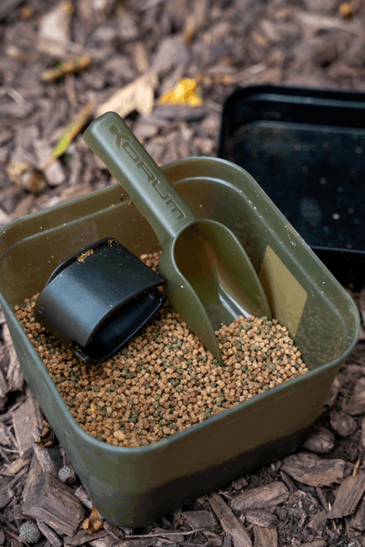 Korum Bait Scoop Small – aasschep in een aasbak met pellets en een methodfeedermal