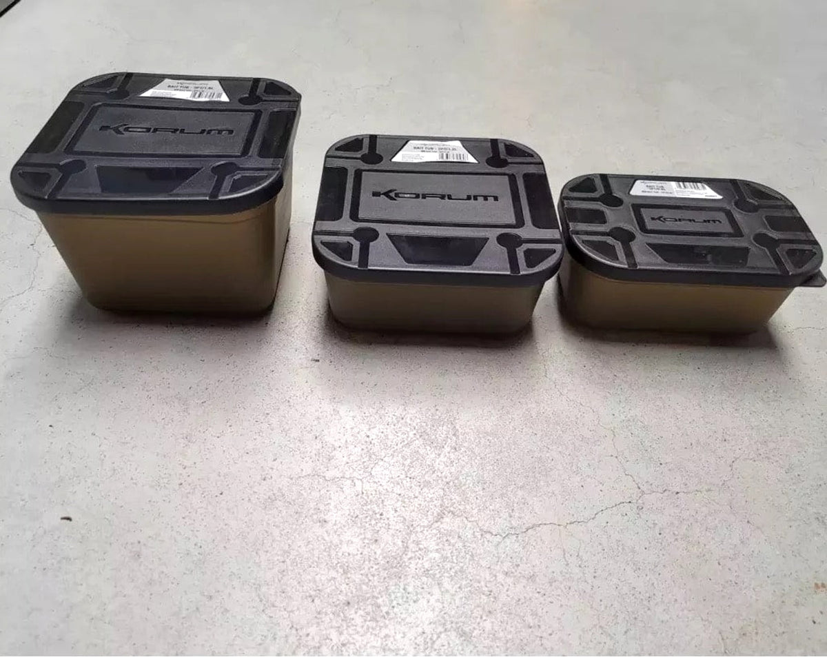 Drie gesloten Korum Bait Tubs met zwarte deksels en productstickers op een grijze ondergrond