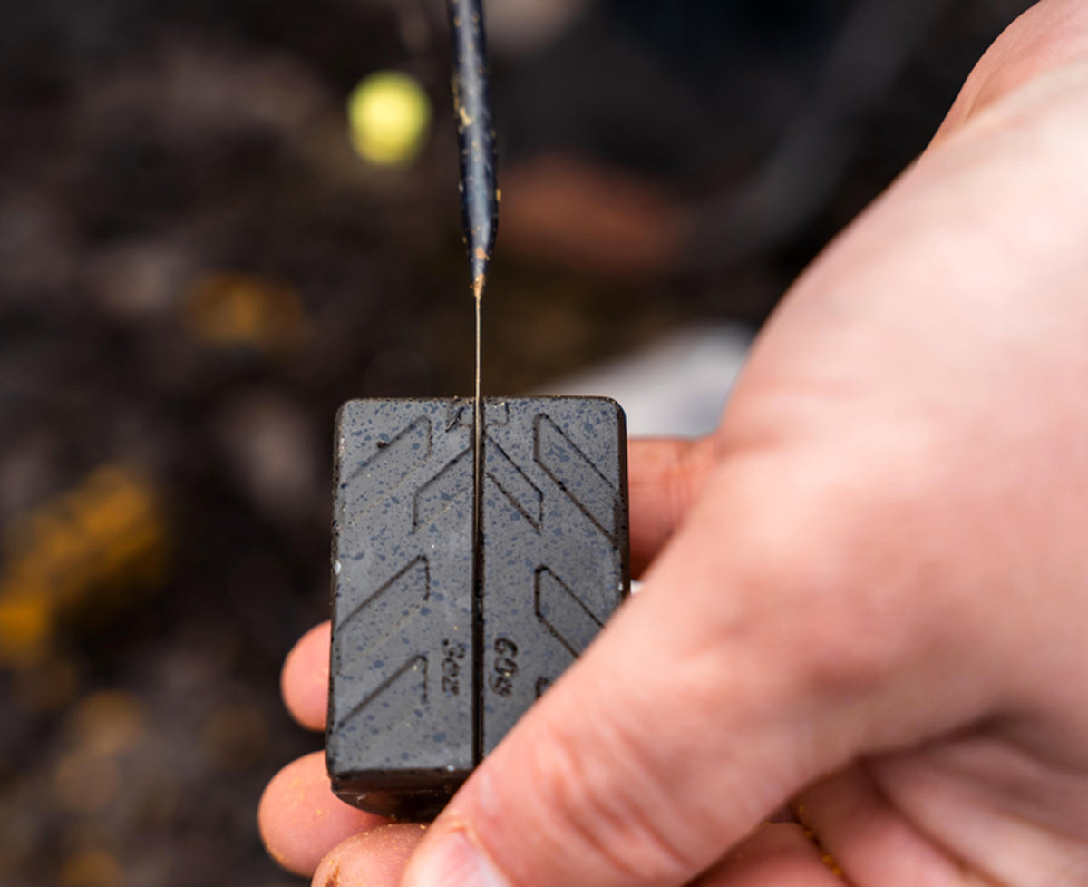 Korum Camo Inline Cage – onderzijde van de voerkorf in de hand, met lijn en inline-insert zichtbaar