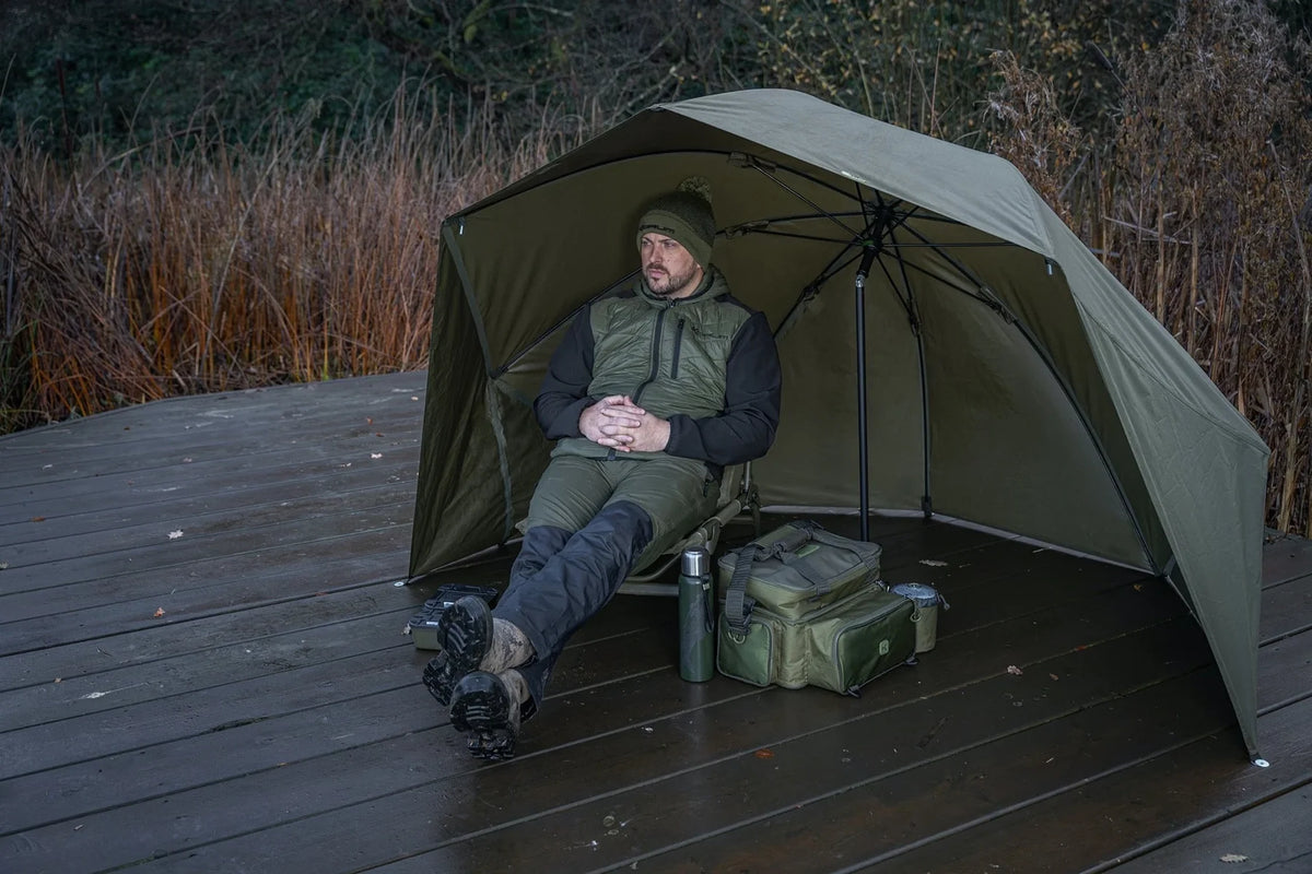 Korum Progress Graphite Brolly Shelter 50 inch – open groene shelter met visser op houten steiger