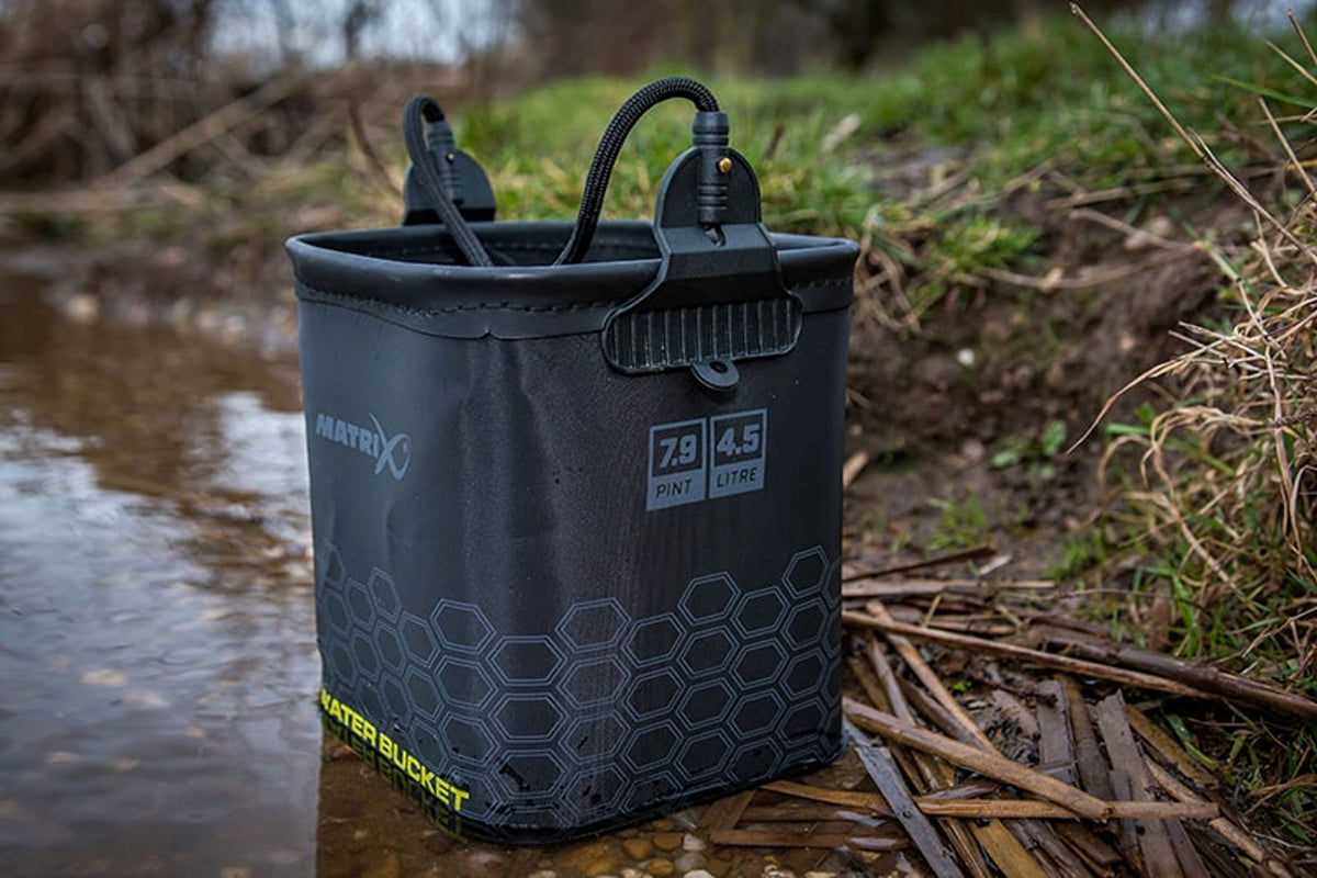 Schuin zijaanzicht van de natte Matrix EVA Water Bucket aan de waterkant, met inhoudsaanduiding