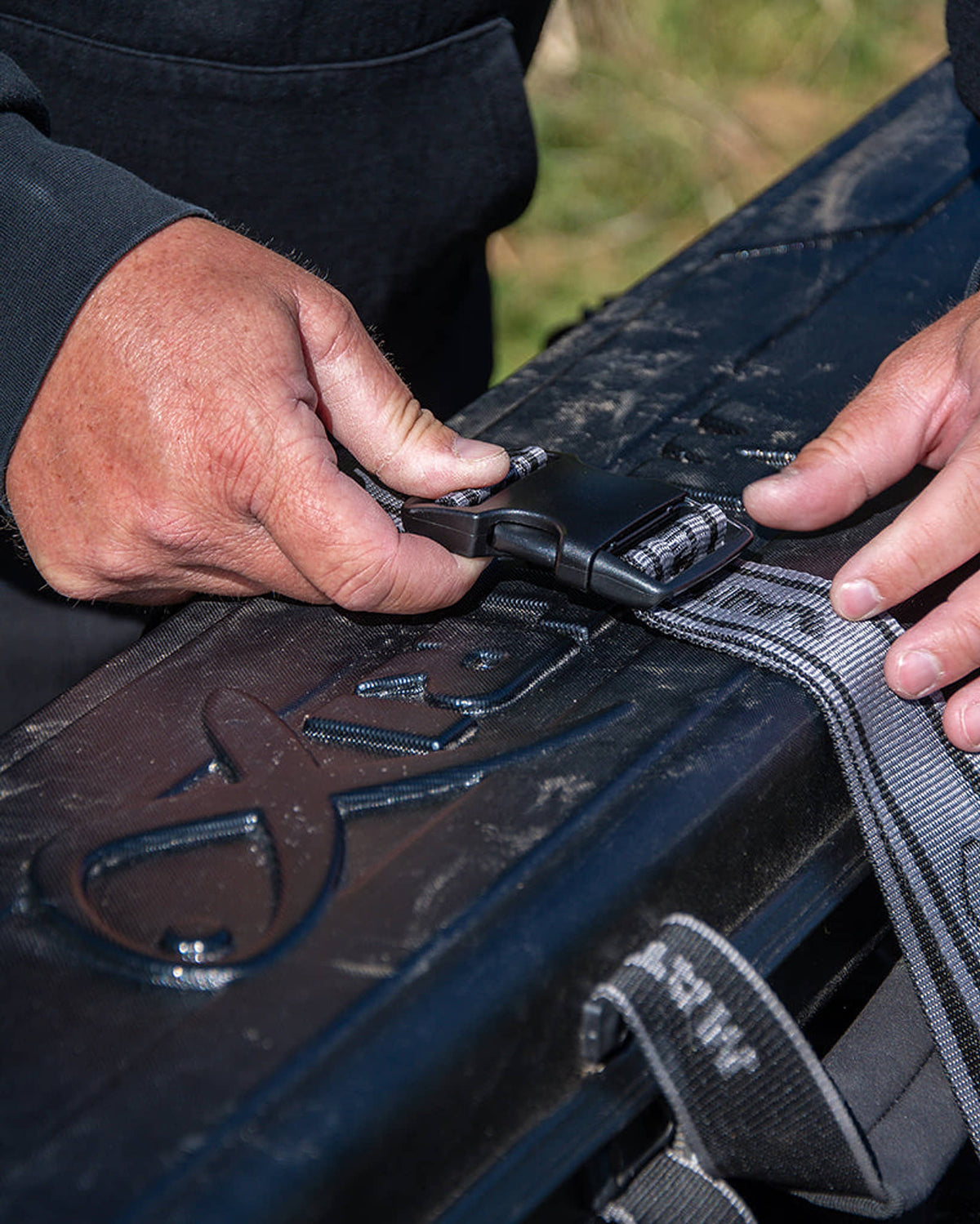 Matrix Adjustable Barrow Straps – de centrale gesp met beide handen sluiten boven een hengelkoffer