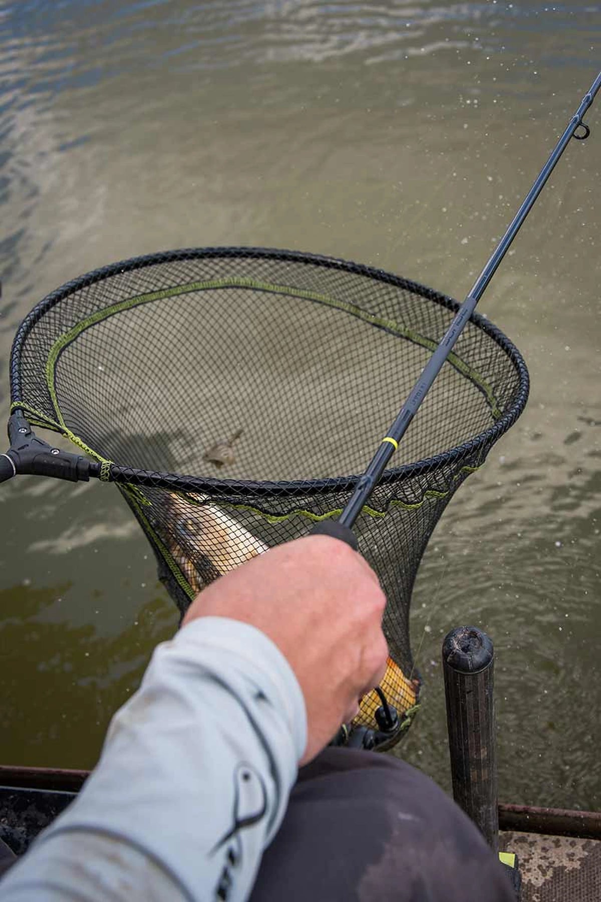 Matrix Aquos Ultra-C Feeder Rod – hengel in de hand boven een schepnet met gevangen karper aan de waterkant