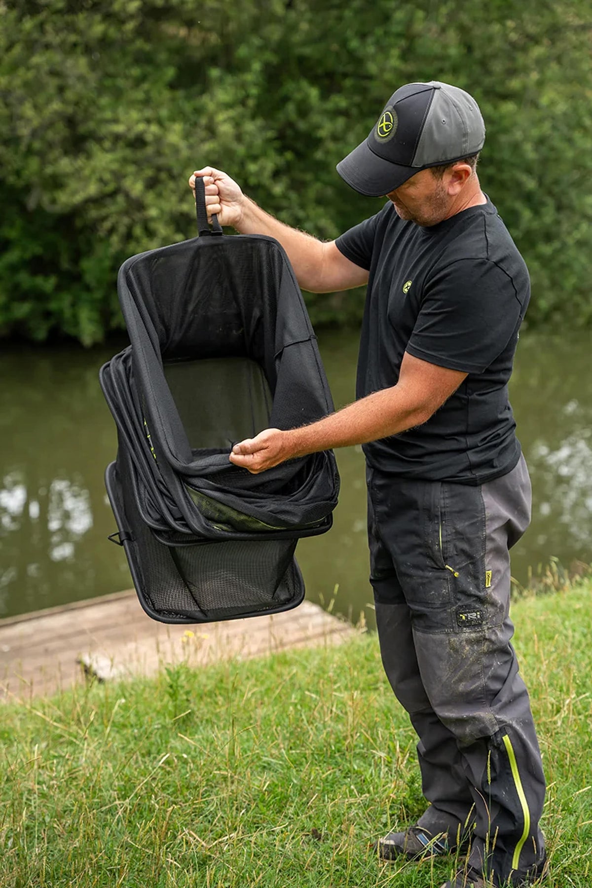 Visser houdt het ingevouwen Matrix Carp Safe leefnet aan de bovenste handgreep en ondersteunt de onderzijde