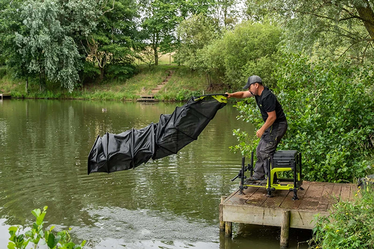Visser laat het Matrix Carp Safe leefnet vanaf een visplatform volledig uitvouwen boven het water