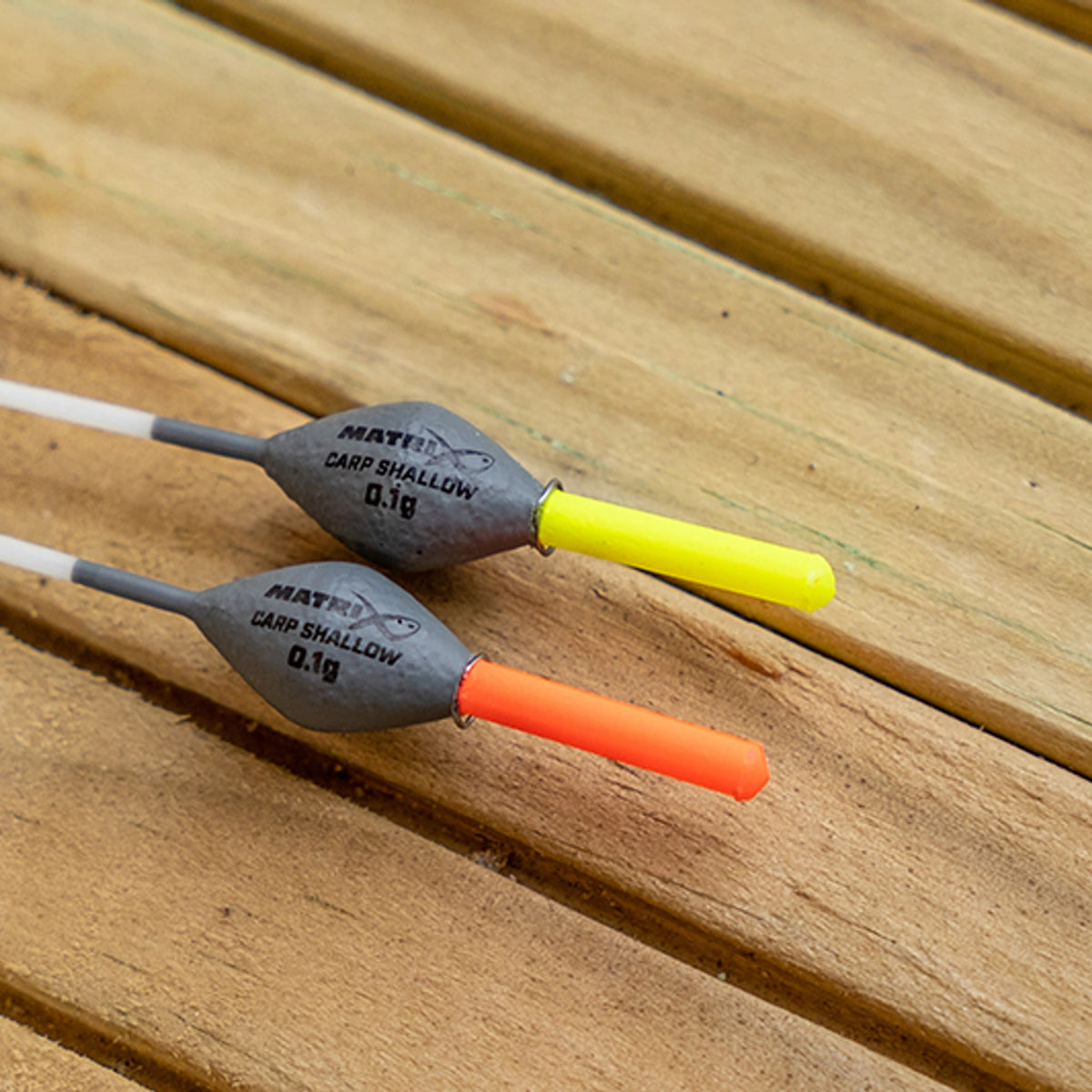 Matrix Carp Shallow Pole Float – 0.1g-dobbers met rode en gele antenne op houten ondergrond
