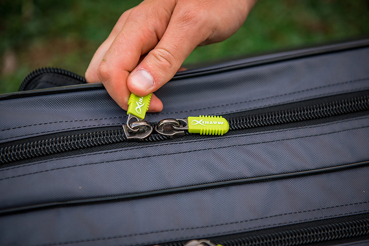 Matrix Ethos Rigid Holdall – hand bedient een gele Matrix-ritstrekker op de zwarte rits van het grijze foedraal