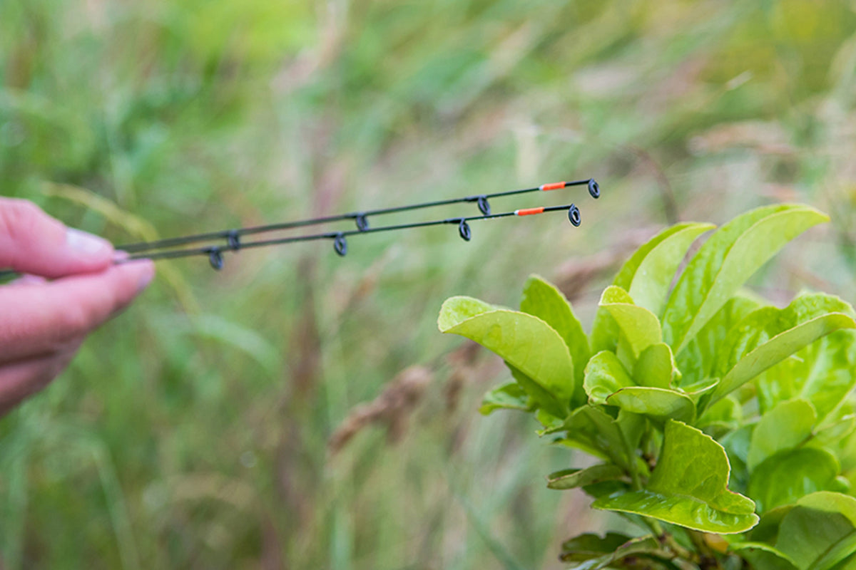 Matrix Ethos XR-C Bomb Rod 9ft – hand toont twee zwarte hengeltoppen met oranje markeringen tegen een groene buitenachtergrond
