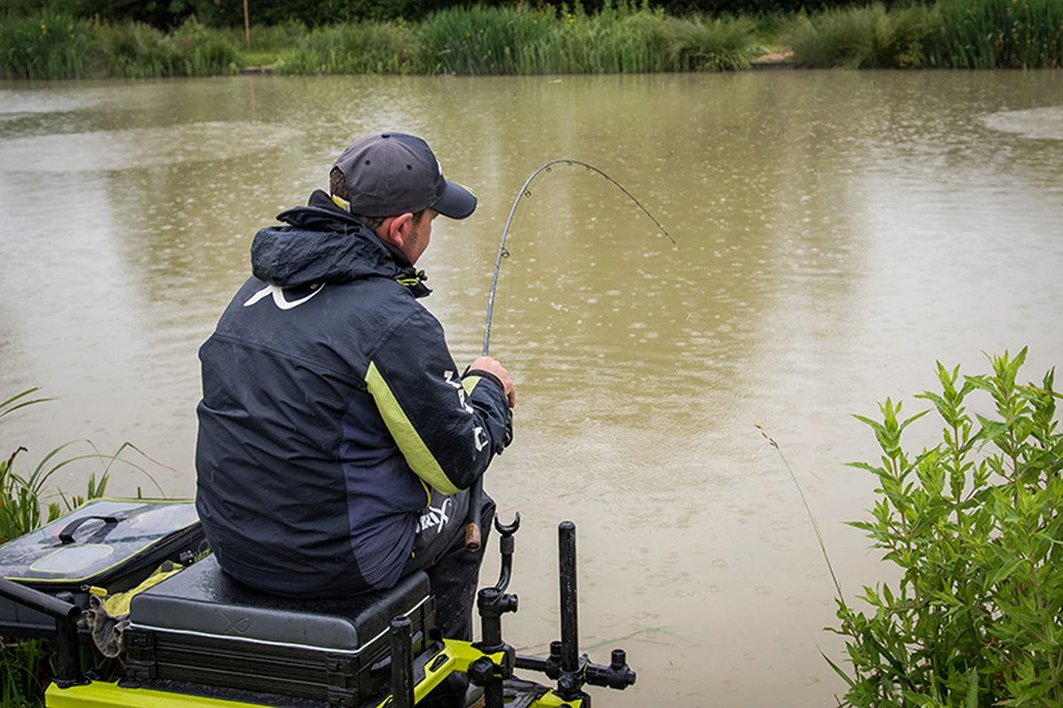 Matrix Ethos XR-C Bomb Rod 9ft – visser op een zitkist aan de waterkant met de hengel gebogen tijdens het vissen