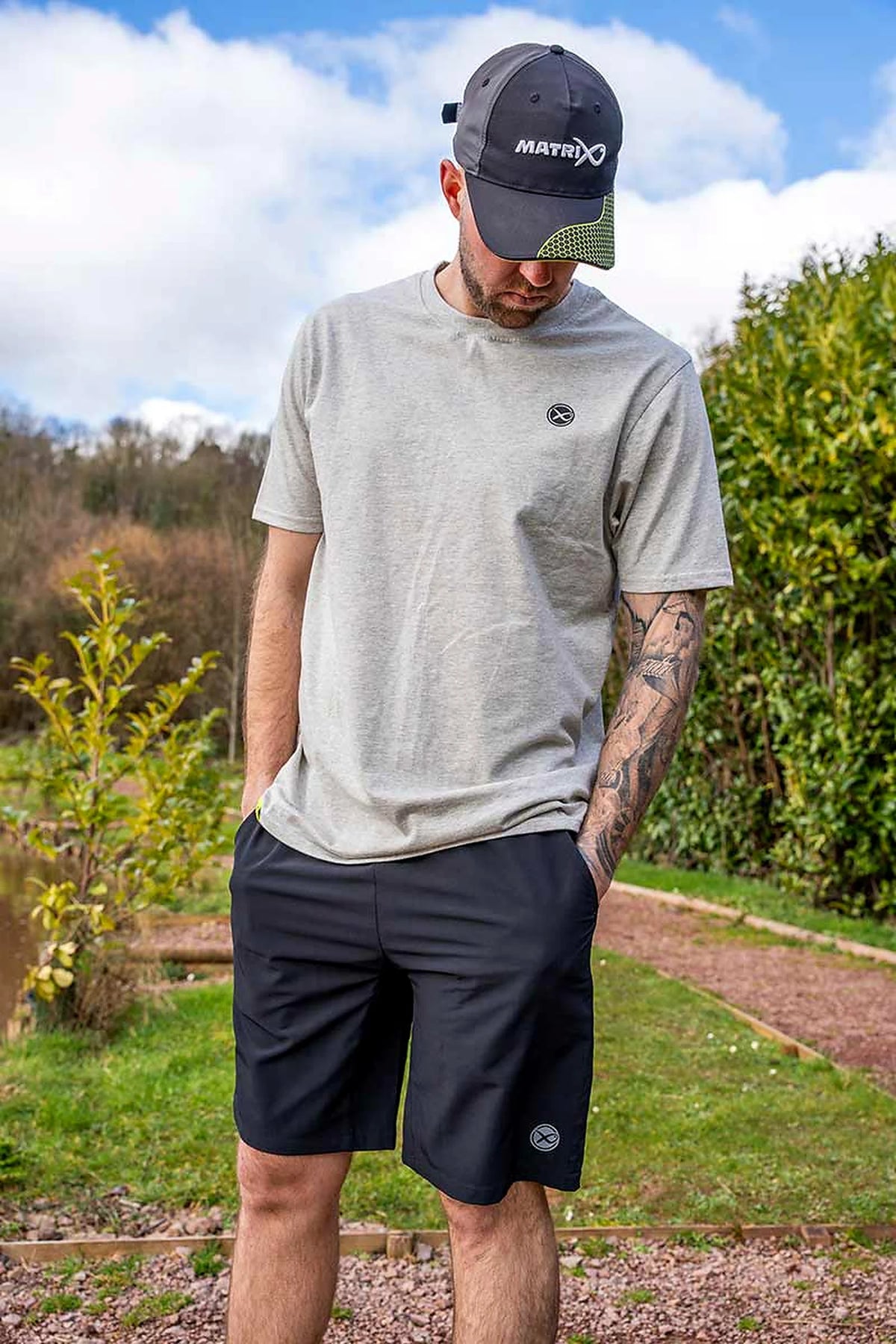 Matrix Grey Mini Logo T-shirt – model met pet toont buiten de voorzijde en pasvorm van het shirt, met handen in de broekzakken