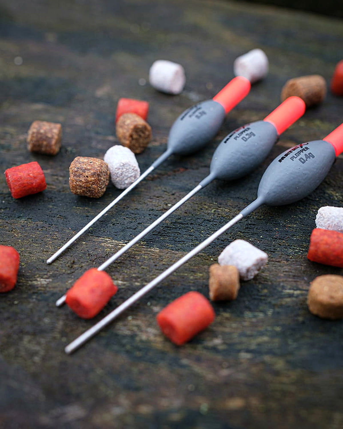 Matrix Plopper Pole Floats – laag aanzicht van drie dobbers en hun onderstelen op hout met losse aasjes