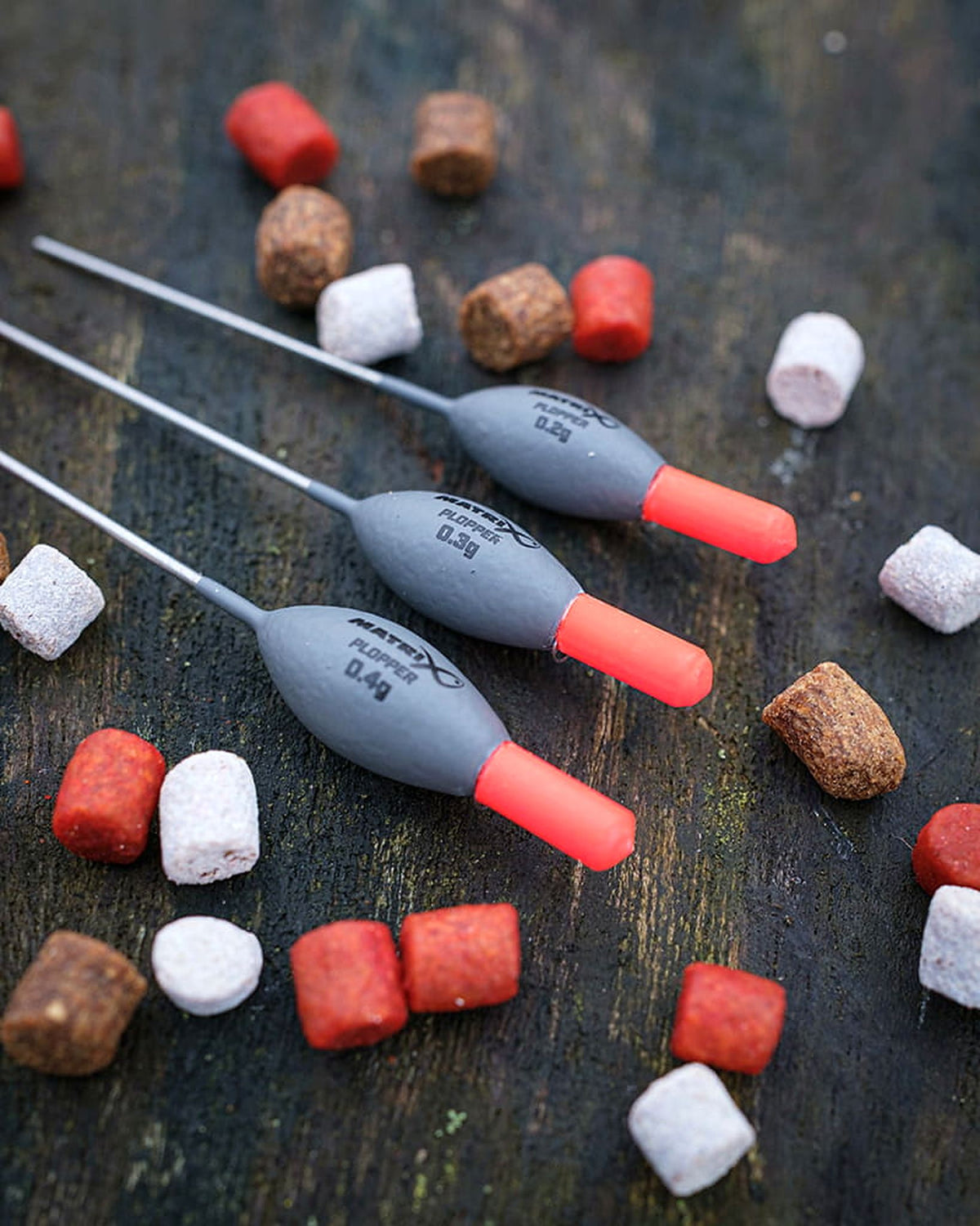 Matrix Plopper Pole Floats – zijaanzicht van drie dobbers op hout tussen gekleurde aasjes