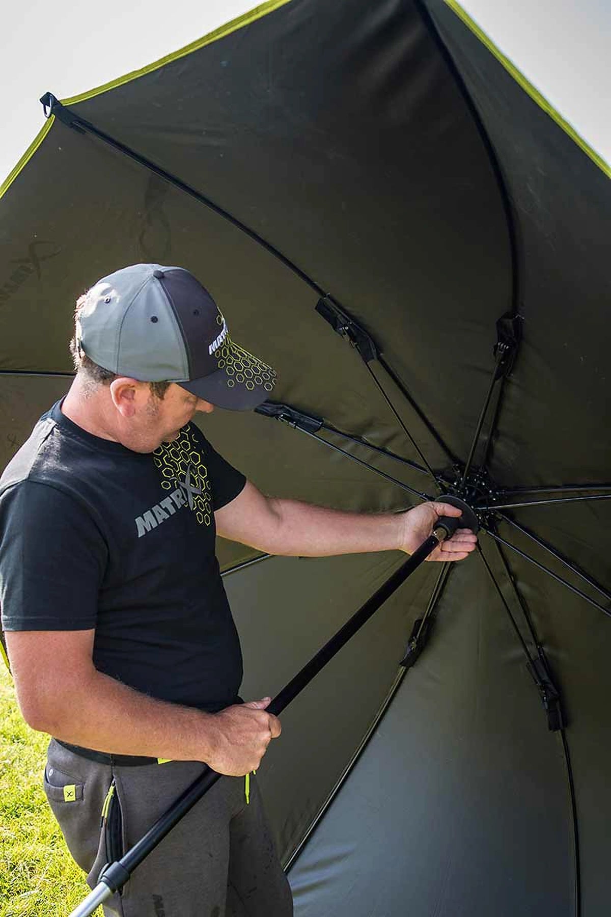 Matrix Pro Over Brolly 45 Inch – visser bedient het centrale mechanisme terwijl hij de steel en het geopende parapluframe vasthoudt