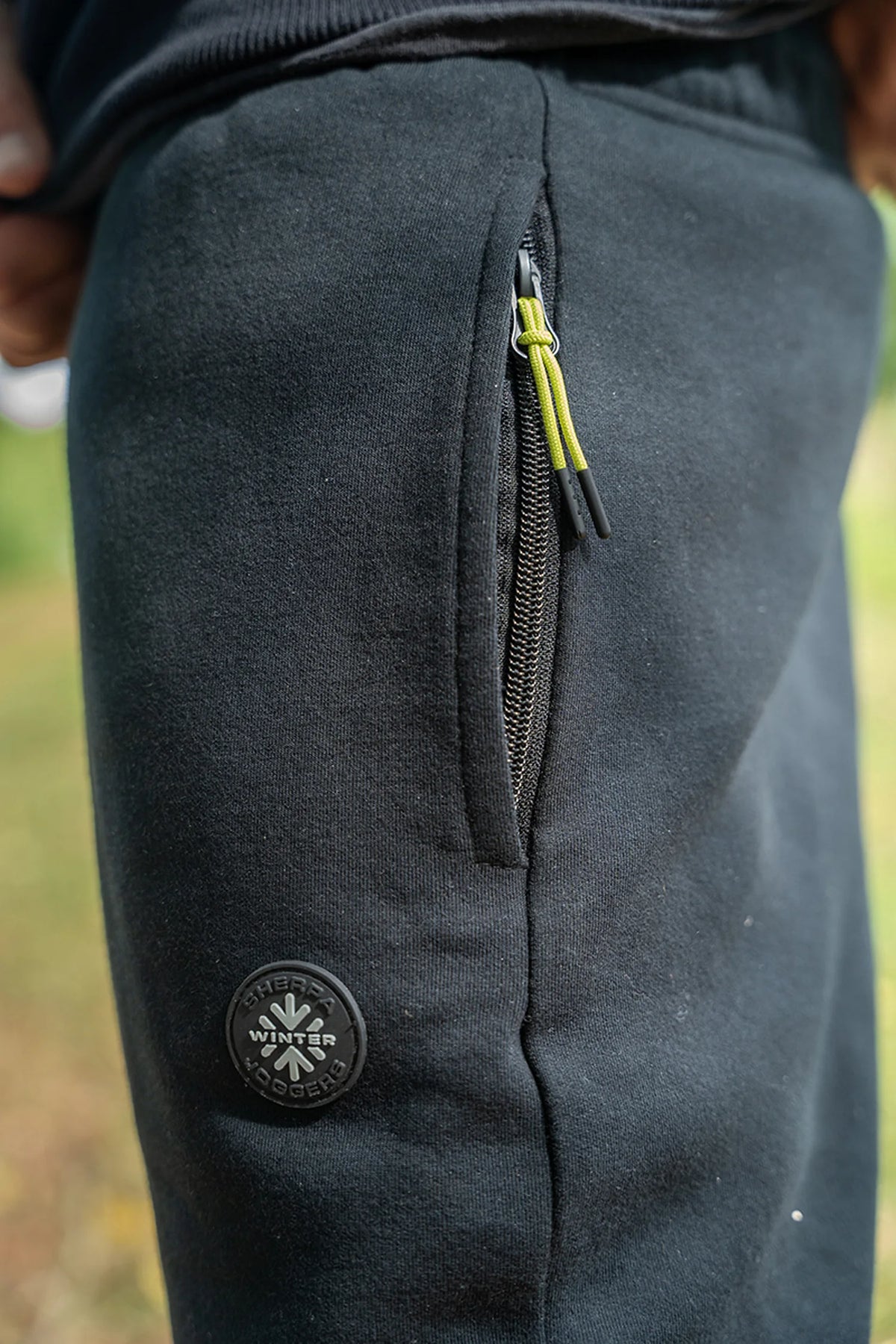 Matrix Sherpa Joggers – zijaanzicht van de gedragen zwarte broek met zakrits, limegroene ritstrekker en ronde badge