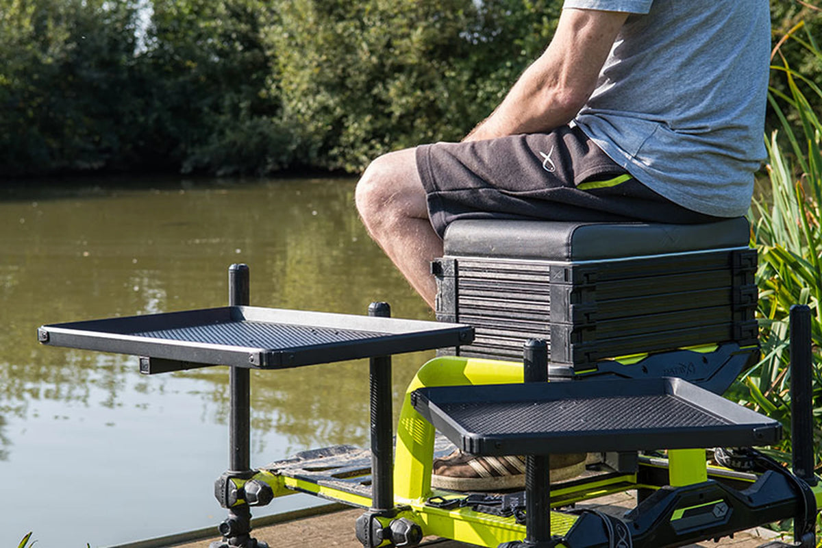 Matrix Standard Side Tray – twee lege aastafels naast een visser op een zitkist aan het water