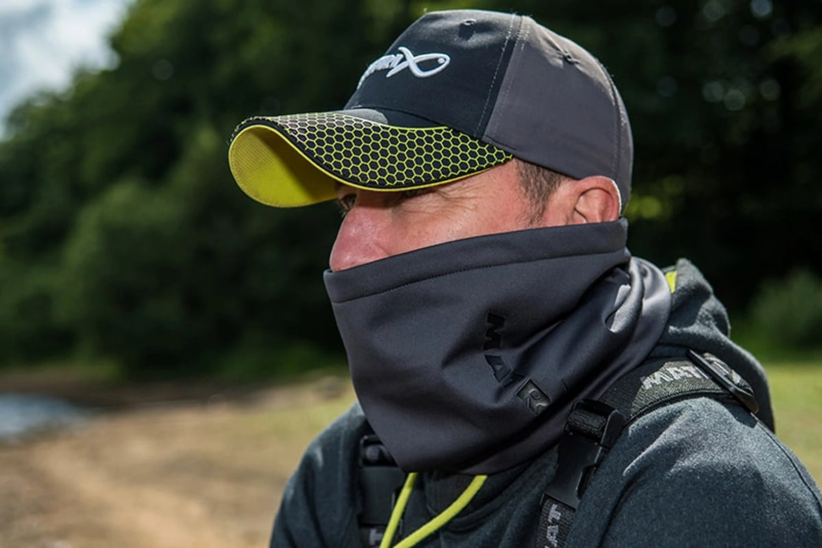 Visser draagt de Matrix Wind Blocker Neck Warmer hoog over de mond aan de waterkant