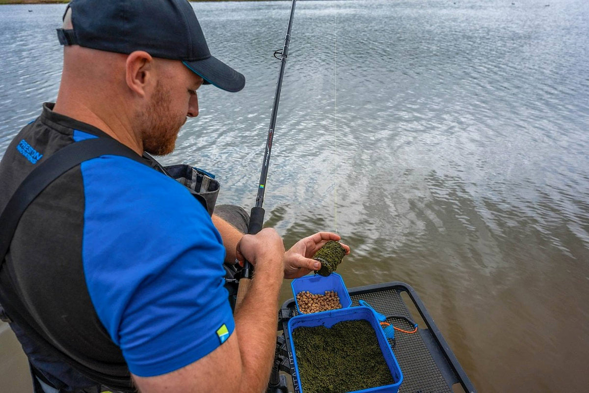 Preston Bait Up Xtreme voerhengel – visser vult een voerkorf boven de voerbak aan de waterkant