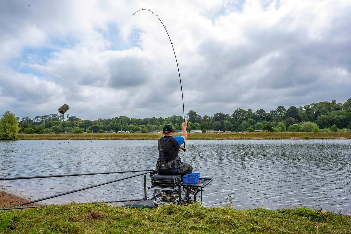 Preston Bait Up Xtreme voerhengel – visser werpt een voerkorf vanaf de zitkist aan de waterkant
