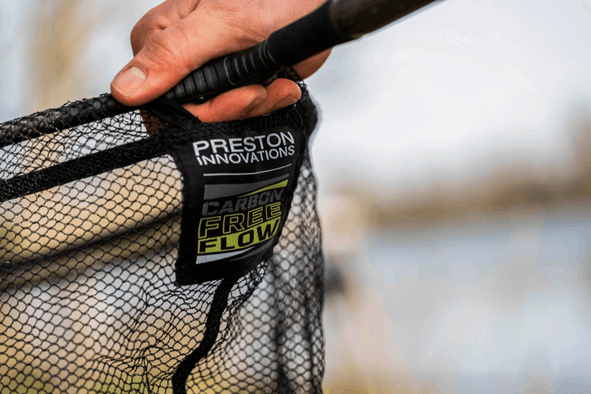 Preston Carbon Free Flow Landing Net vastgehouden bij de aansluiting, met de zwarte netrand, mazen en het Carbon Free Flow-etiket zichtbaar