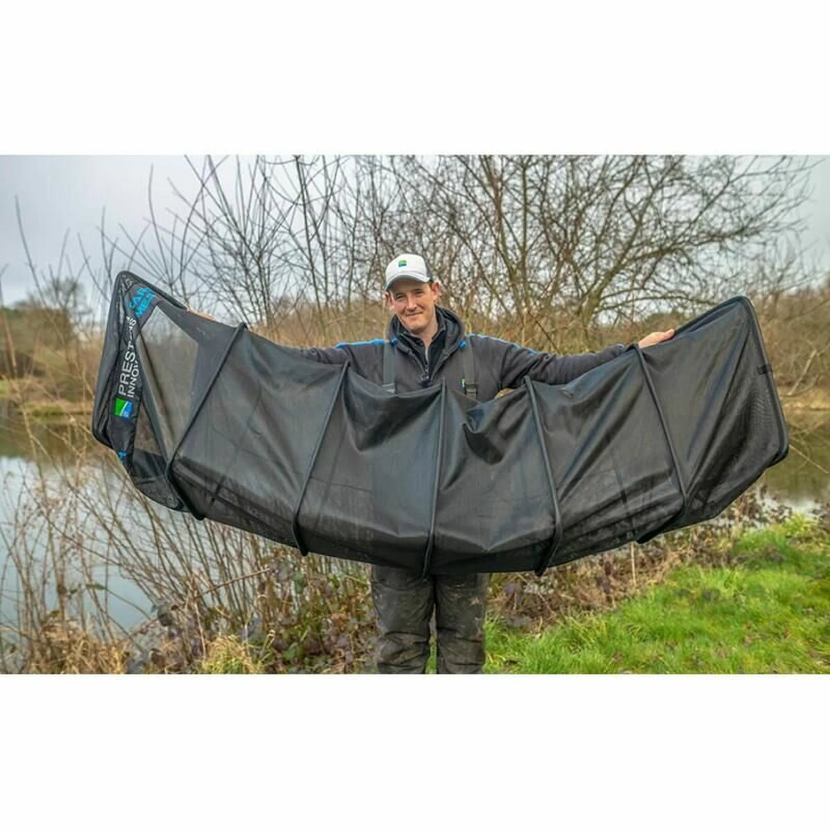 Visser toont de breedte van het Preston Carp Mesh Keepnet aan de waterkant
