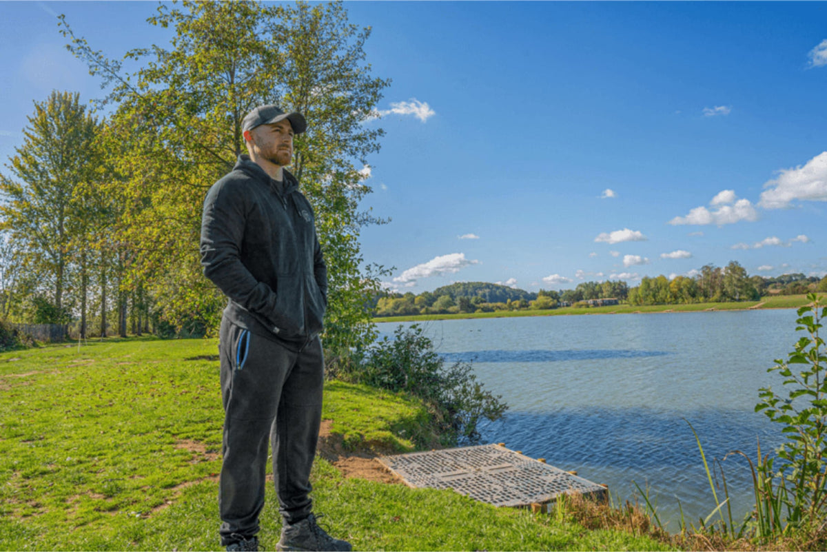 Visser draagt de Preston Core Collection Zip Hoodie aan de waterkant naast een visplatform