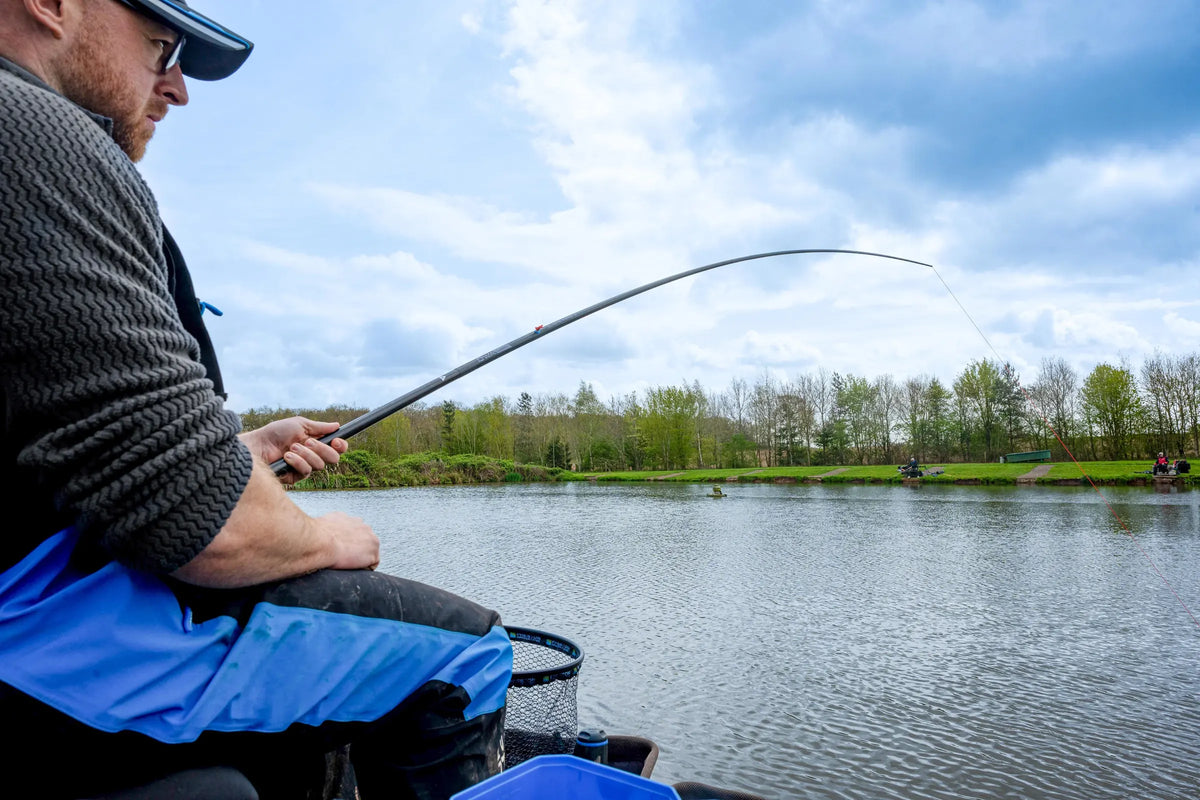 Zijaanzicht van een visser met gebogen Preston DWA Kits Carp-topset en uitgerekt rood elastiek boven het water