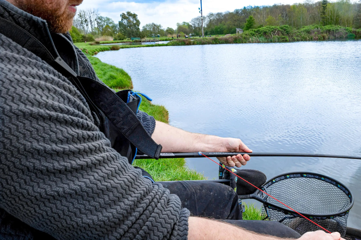 Visser gebruikt de Preston DWA Kits Carp-topset aan de waterkant, met rood elastiek dat door de blauwe Roller Pulla-opening loopt