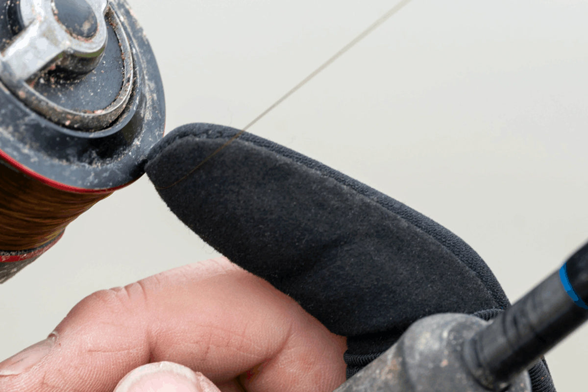 Detail van de zwarte Preston Extremity Finger Stall met vislijn over de beschermde vingertop naast een molenspoel