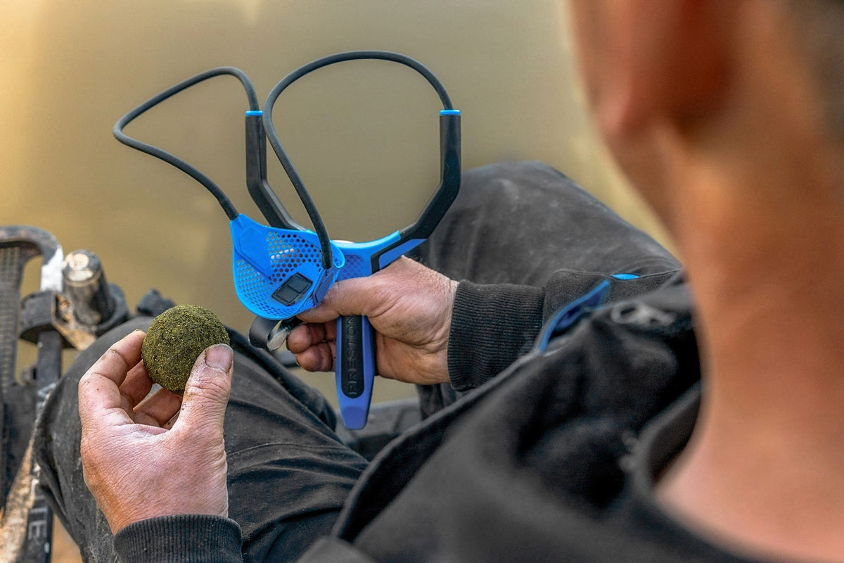 Visser houdt een voerbal naast de Preston Groundbait Catapult, klaar om de pouch te vullen