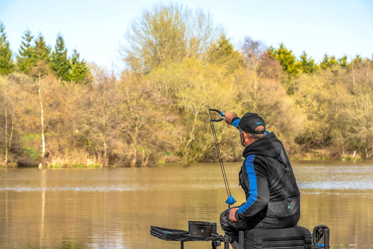 Visser gebruikt de Preston Groundbait Catapult vanaf een zitkist aan het water