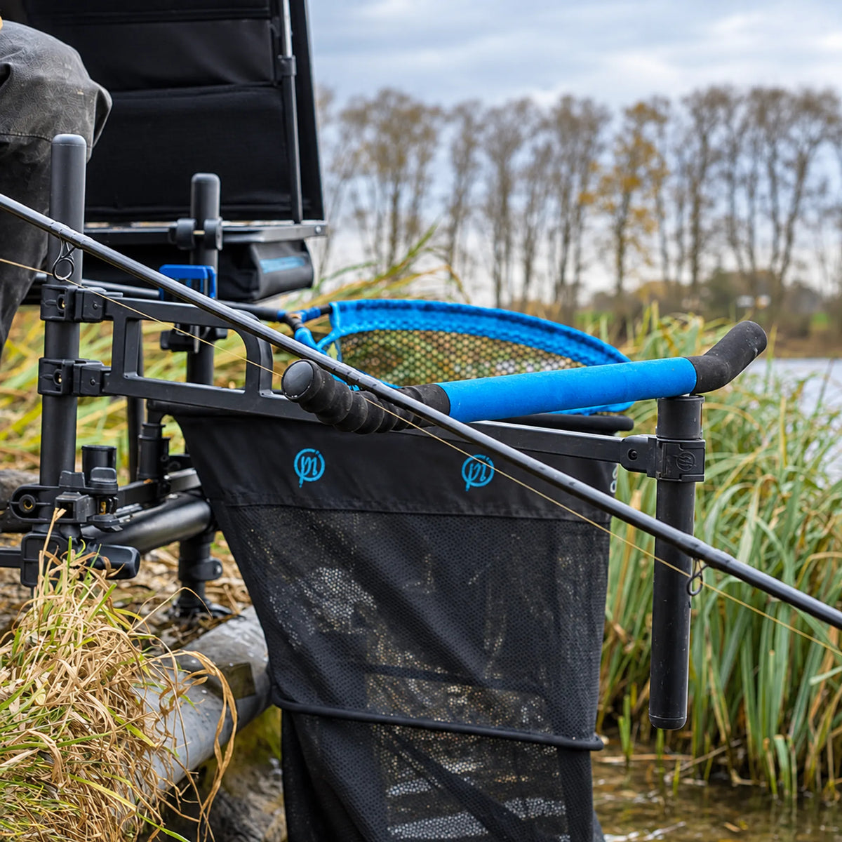 Preston Offbox 36 Pro Feeder Arm gemonteerd op een zitkist met feederhengel en blauw schepnet aan de waterkant