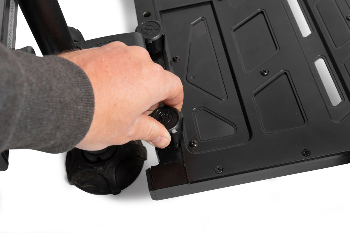 Een hand bedient de zwarte draaiknop van de Preston Offbox Side Foot Rest, naast de voetplaat met uitsparingen en schroeven