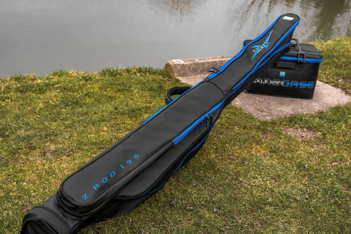 Preston Supera X 2 Rod 195-foedraal aan de waterkant, met lang buitenvak en blauwe ritsranden, steunend op een Tackle Safe-tas