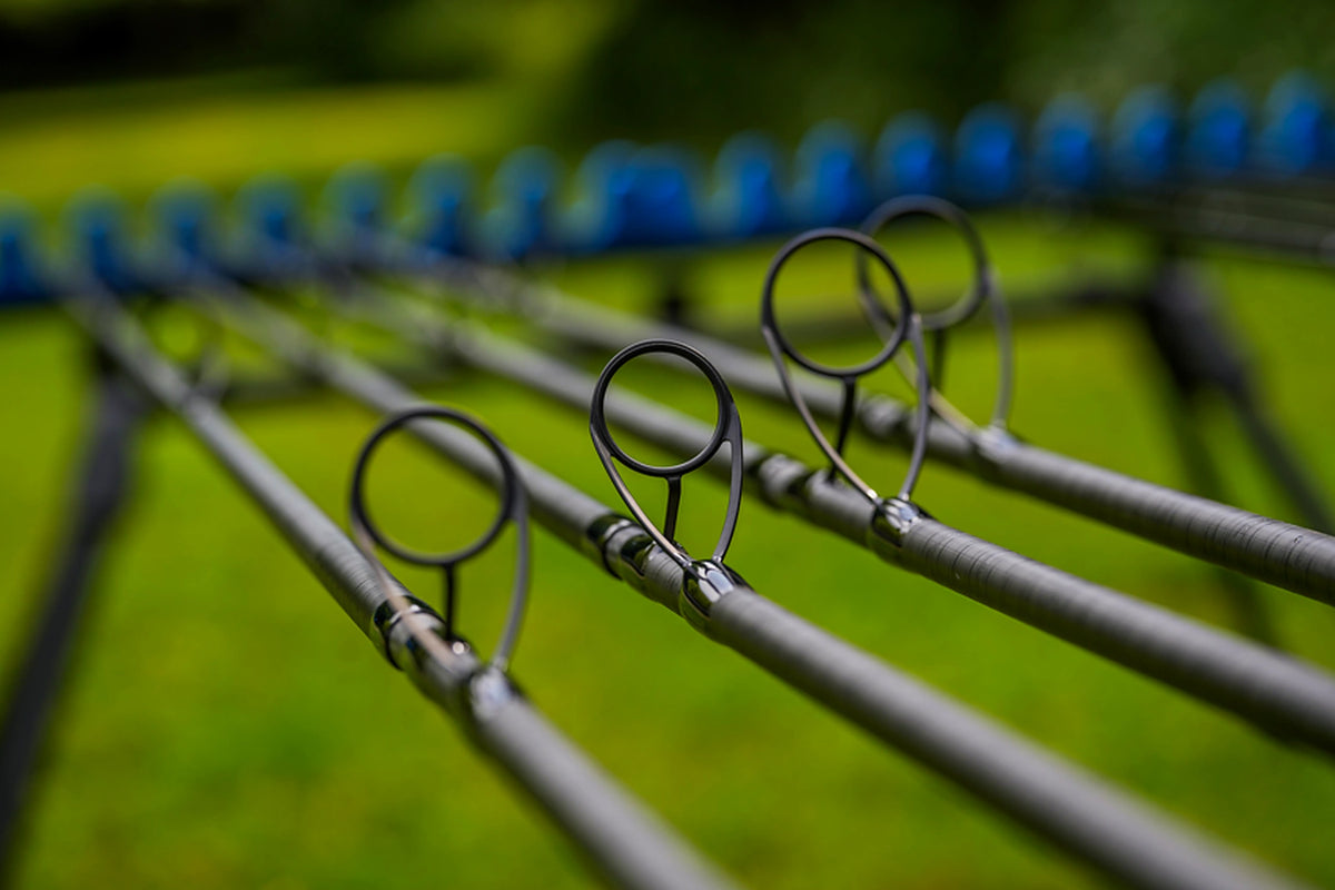 Preston Supera X Distance Feeder – vier grote zwarte geleideogen op de carbon hengeldelen, uitgestald op een blauwe hengelsteun