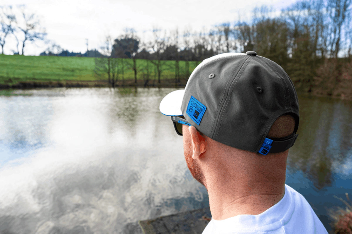 Preston White Drift Cap gedragen van achteren, met verstelband en blauw label zichtbaar bij het water