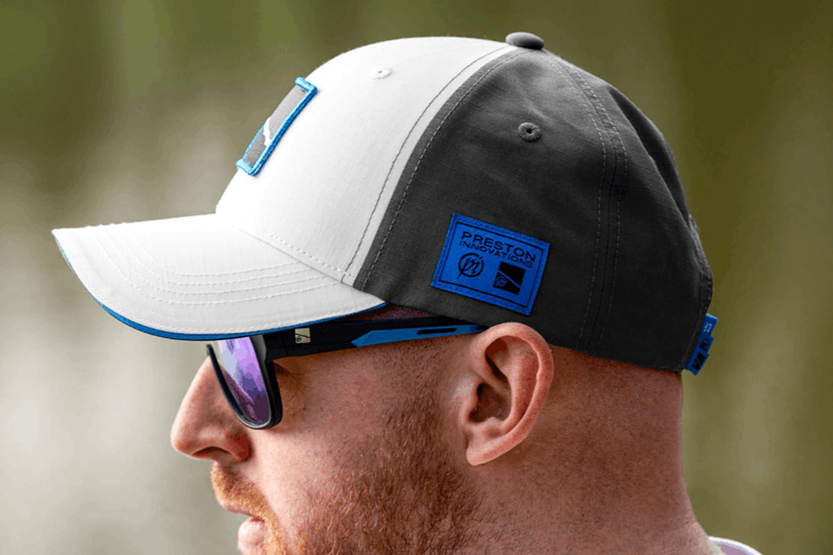 Preston White Drift Cap gedragen in detail van opzij, met blauw Preston-label en blauwe kleprand